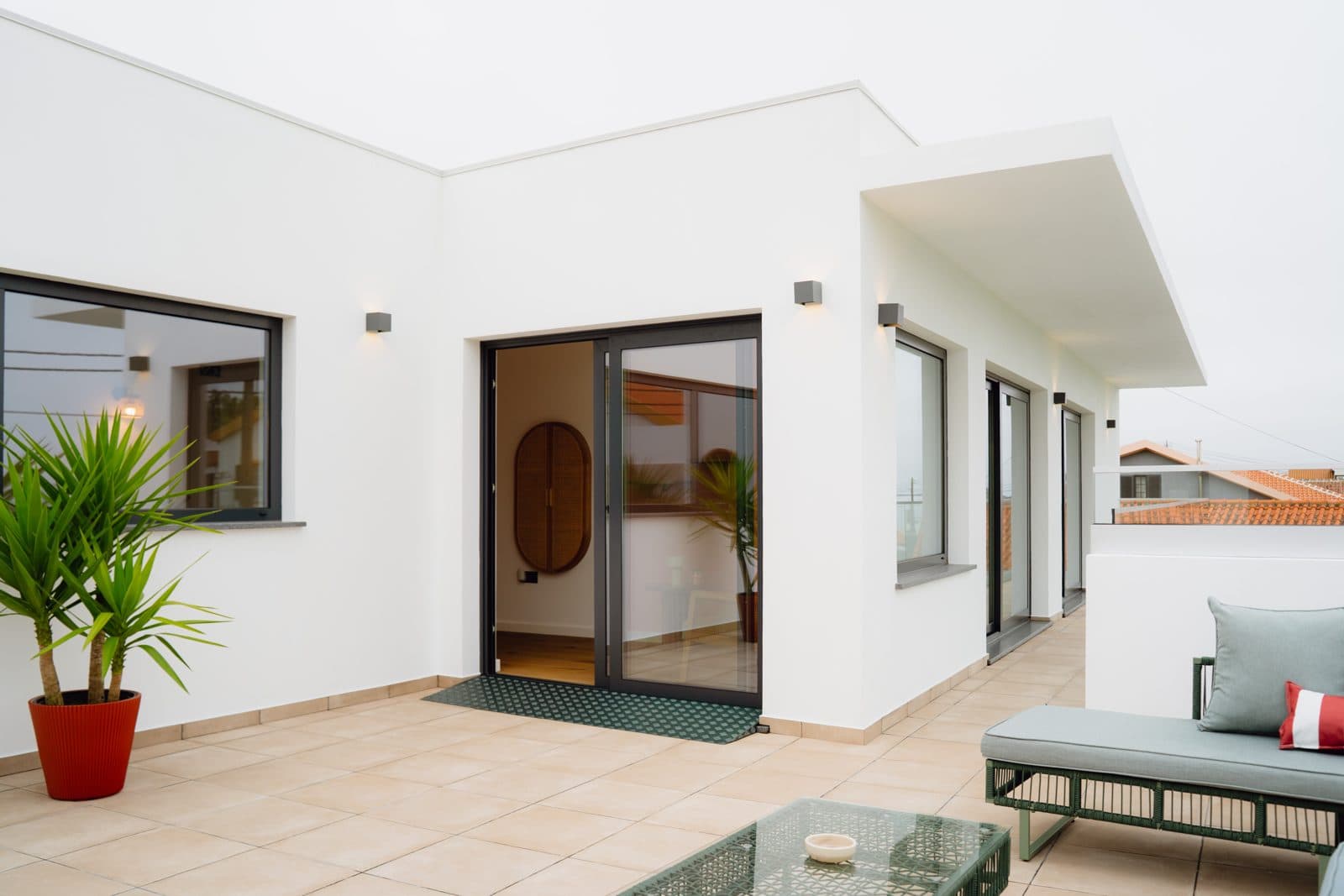 Exterior do Terrassi Villa: volumes brancos com a placa da casa em verde, terraço pavimentado com sofá e porta de correr para o interior, e em redor o pasto e os muros de pedra basáltica da costa norte da Terceira — vista 3