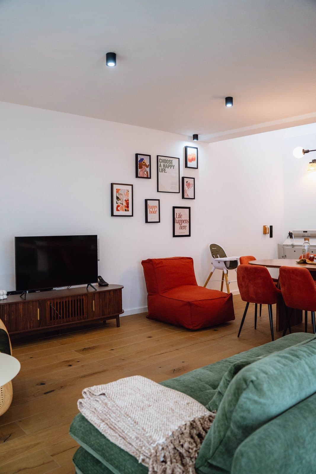 Open space do Terrassi Villa: cozinha verde com bancada corrida em madeira, mesa de refeição posta e, sob a escada de ripado, um recanto de brincar com banca de mercado, cozinha de madeira e livros infantis — vista 3