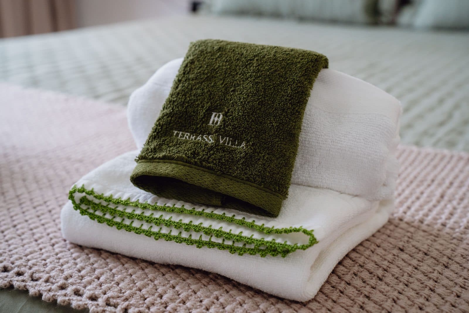 Quarto do Terrassi Villa: cama de casal com colcha verde-seiva e almofadas de folho, cabeceira estofada, mesinhas suspensas em madeira com candeeiro aceso, e porta de correr para uma varanda com guarda de vidro sobre o pasto — vista 3