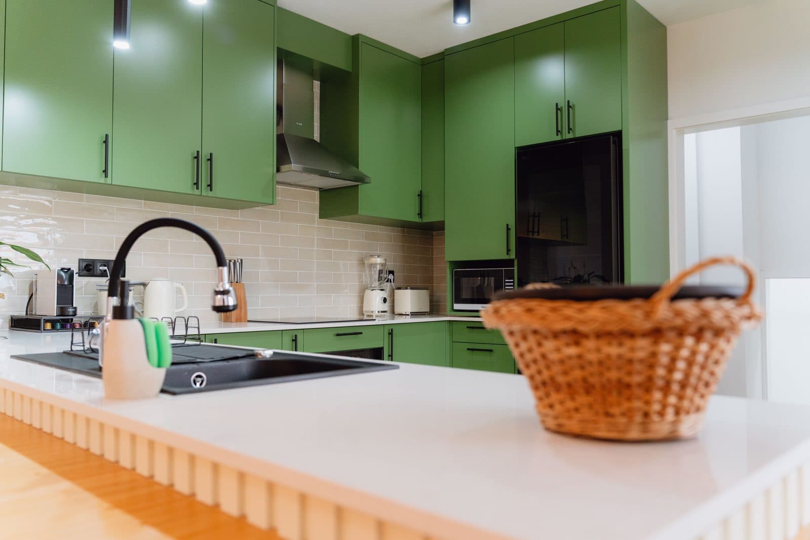 Cozinha adaptada do Terrassi Villa: armários verdes em U, azulejo bege brilhante, forno encastrado, placa de indução e exaustor; à esquerda, um troço de bancada com espaço livre por baixo, e uma gaveta funda aberta com tachos ao alcance da mão — vista 2