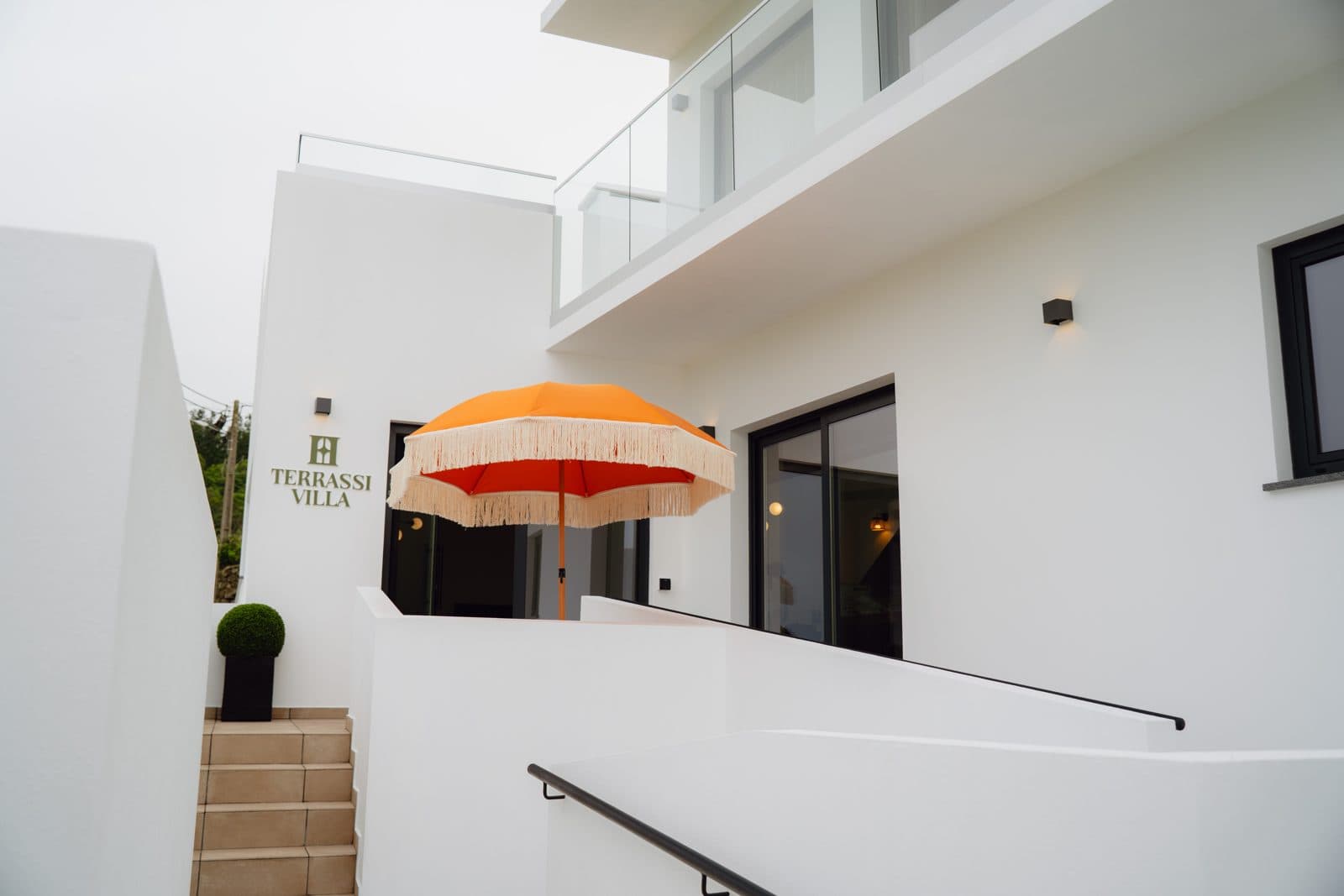 Terraço do Terrassi Villa: bancada exterior com lava-loiça e remate em azulejo verde, três bancos altos de verga, e forno de lenha em tijolo com arco e lenha empilhada por baixo da bancada — vista 3